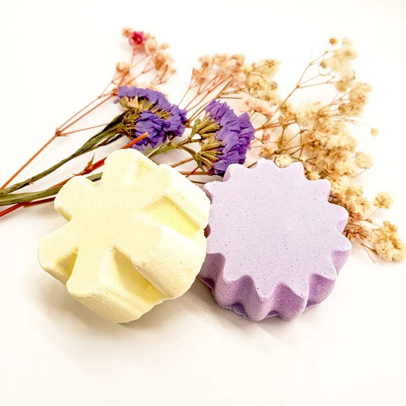 Two bath bombs, one yellow and one purple, placed beside dried flowers.