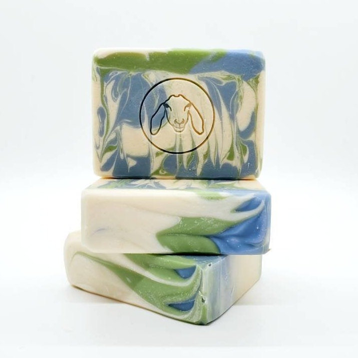 Three bars of marbled soap with green, white, and blue swirls, and a goat logo embossed on the top bar.