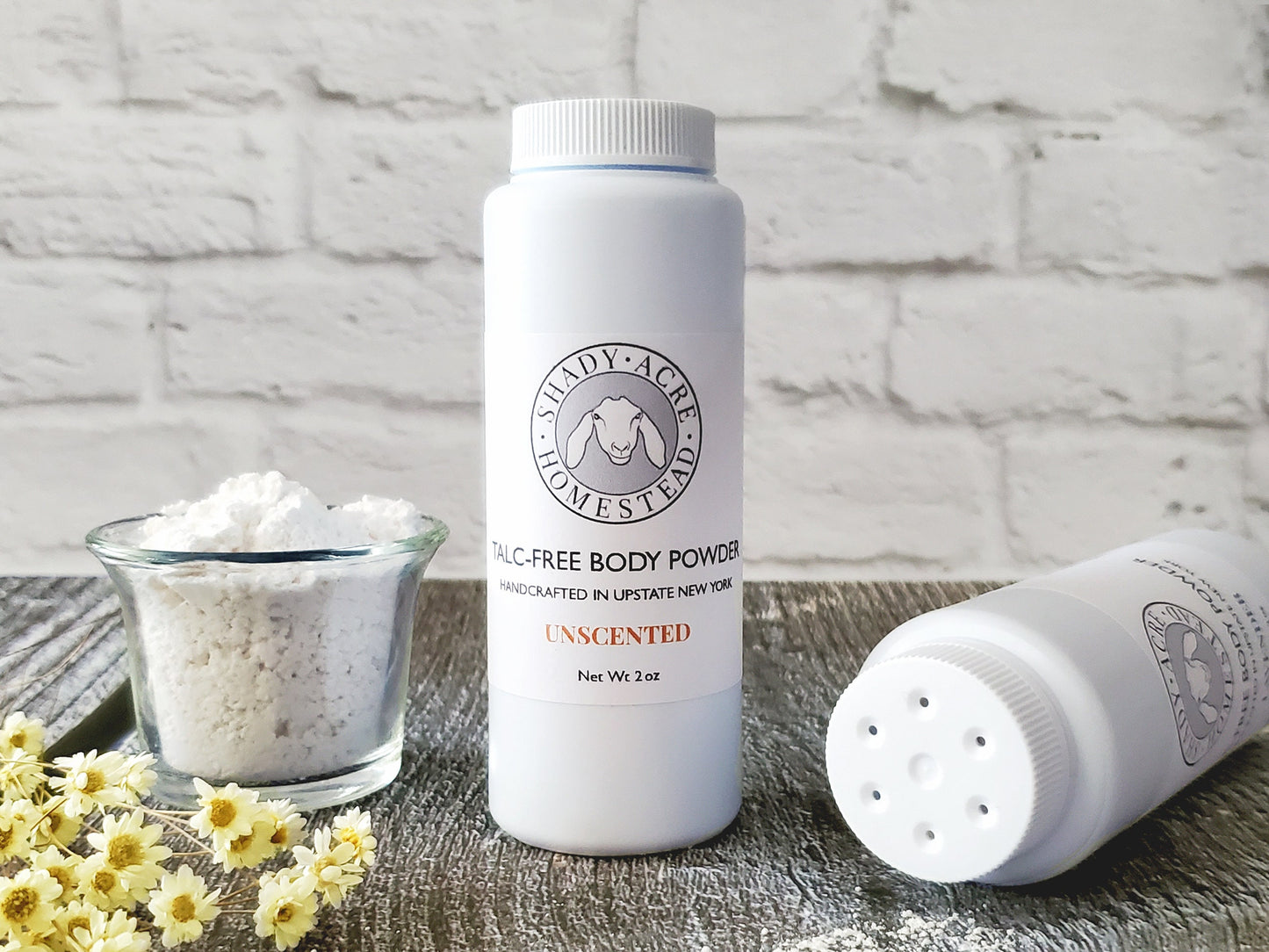 Talc-free body powder bottle with a small bowl of powder and flowers